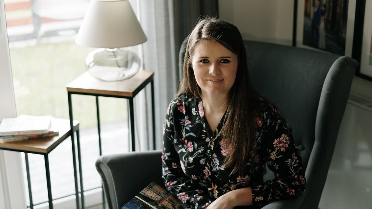 Brunette woman sitting comfortably in an armchair, enjoying a book in a cozy, well-lit living room.